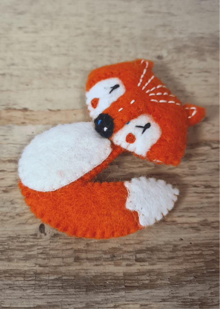 felt orange fox finger puppet with white belly eyes and tail end and black nose sat on wooden surface