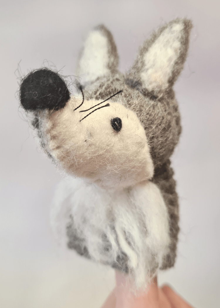 close up of a felt grey and white wolf finger puppet with black nose, whiskers and bead eyes sat on someone&