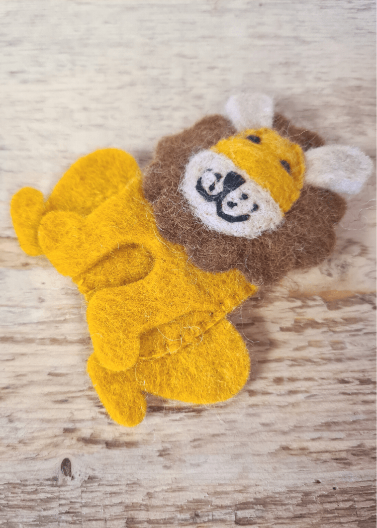 sitting felt yellow lion finger puppet with brown mane and smiley face laying on a wooden surface