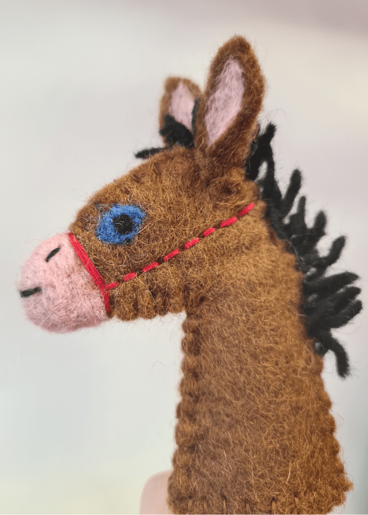 close up of a brown felt horse finger puppet with a black main, pink nose, blue eye and red bridle