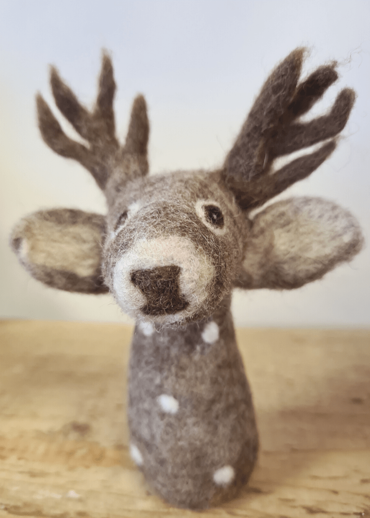 close up of a grey felt deer finger puppet with white spots, brown antlers and nose, a cute face and big ears sat on a wooden surface
