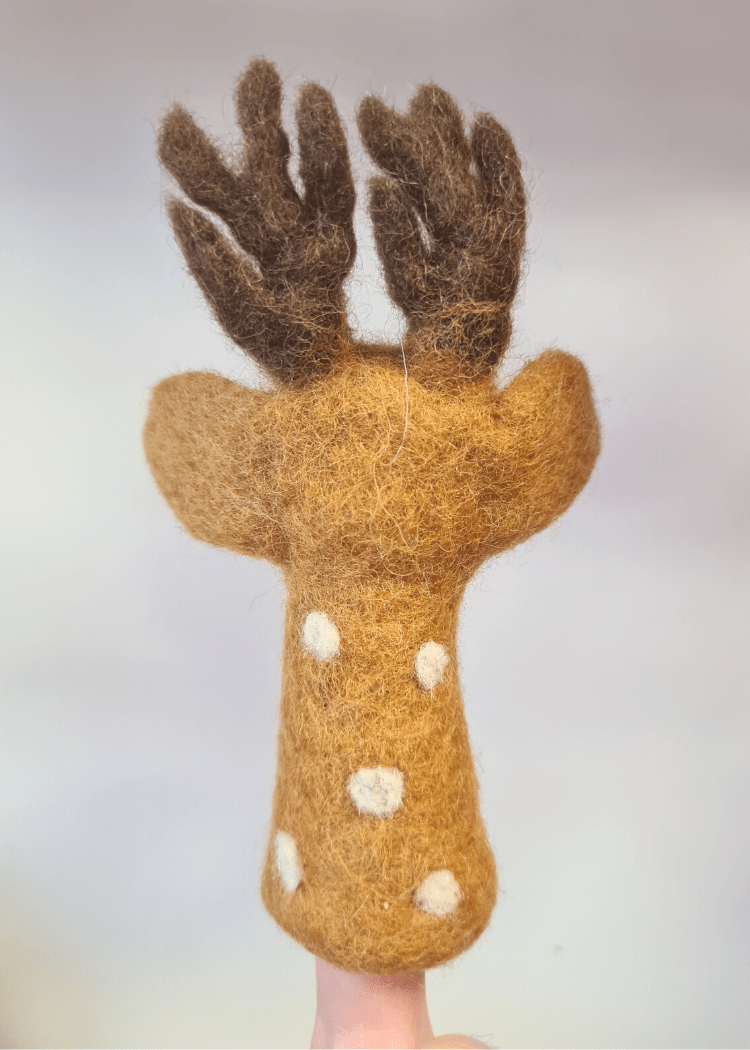 back of a tan brown felt finger puppet with white spots and dark brown antlers sat on someones finger