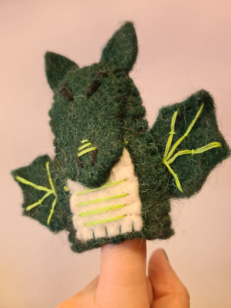 Side angle close up of Elefair Giftware green felt dragon finger puppet with white chest and yellow thread in wings sitting on a finger