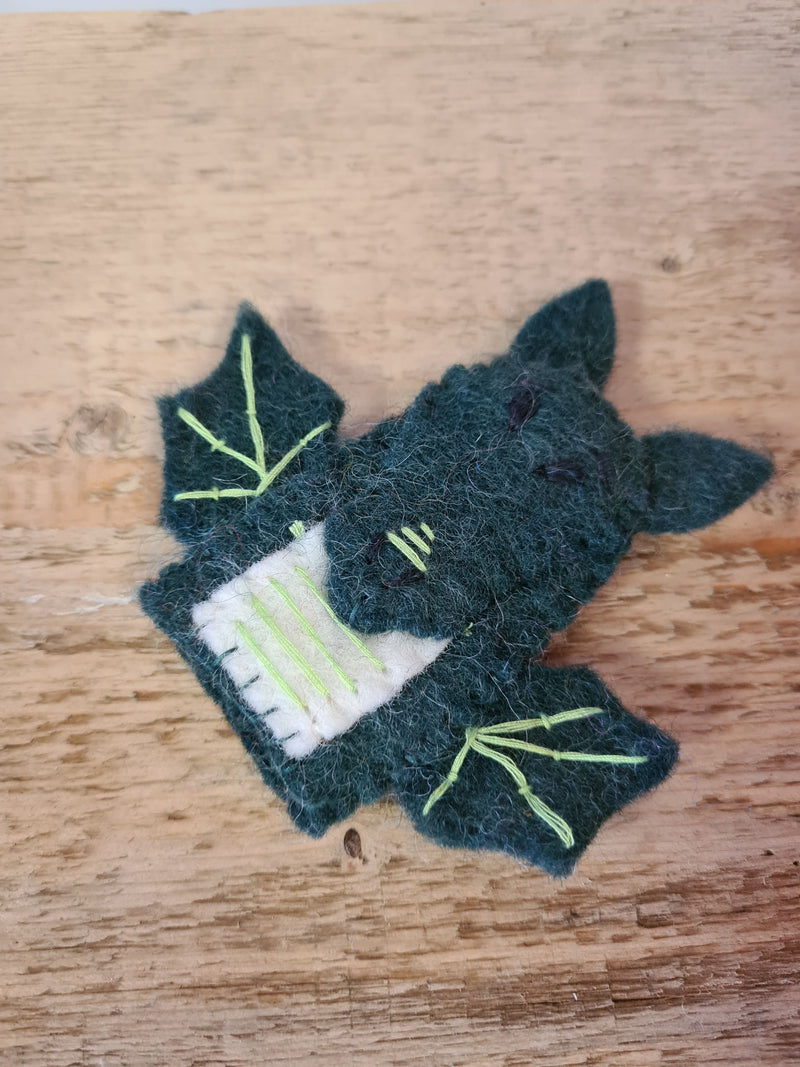 Elefair Giftware green felt dragon finger puppet with white chest and yellow thread in wings laying on a wooden surface