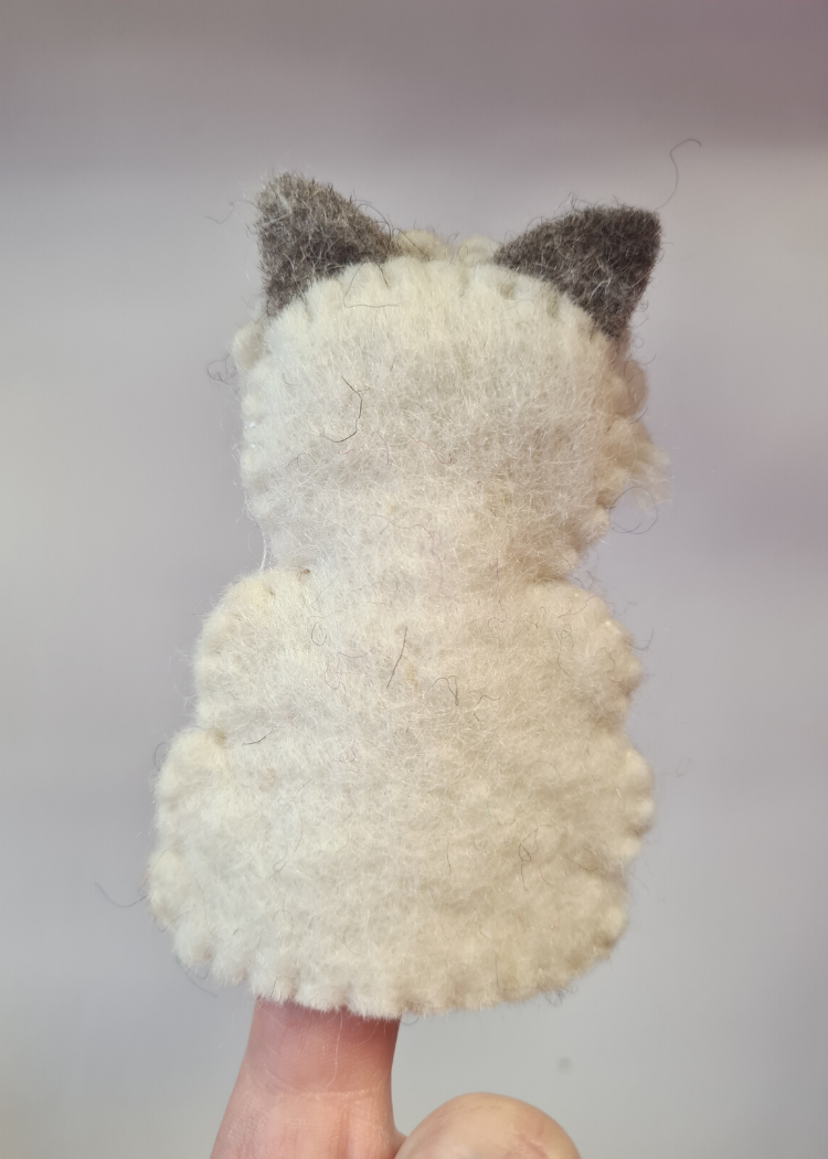 the back of a felt white sheep finger puppet with cute grey face and ears sat on someones finger