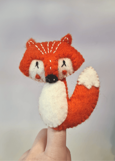 felt orange fox finger puppet with white belly eyes and tail end and black nose sat on someones finger