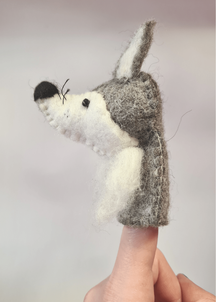 side view of a felt grey and white wolf finger puppet with black nose, whiskers and bead eyes sat on someone&
