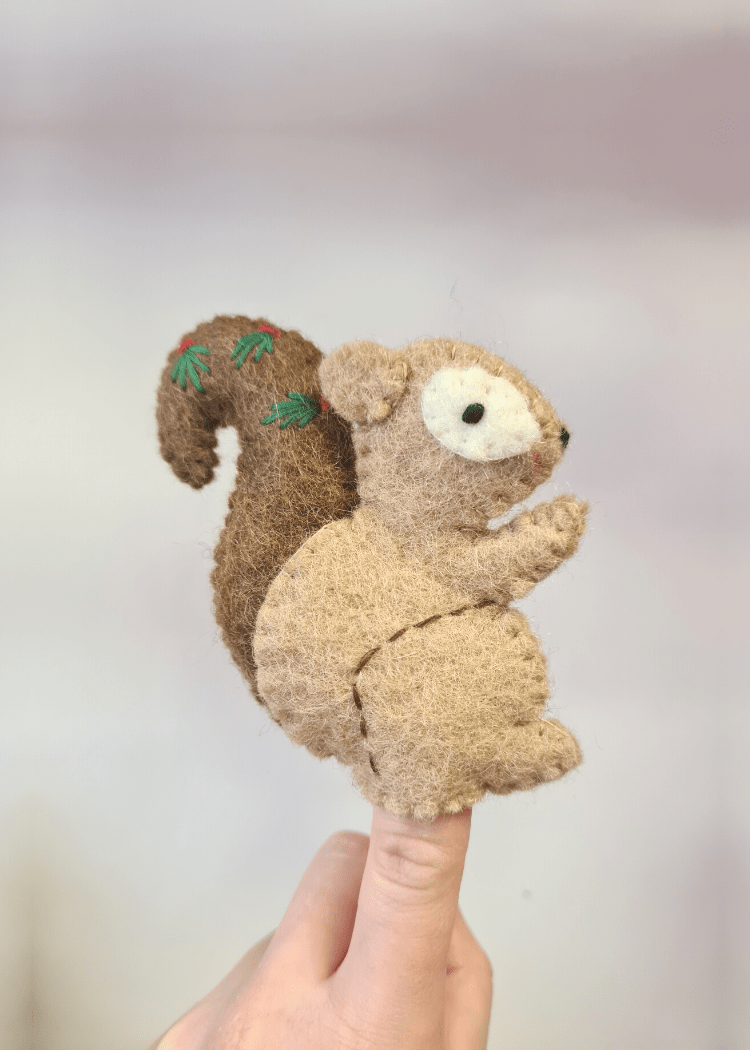 light brown felt squirrel finger puppet with dark brown tail and leaves on, sat on someones finger