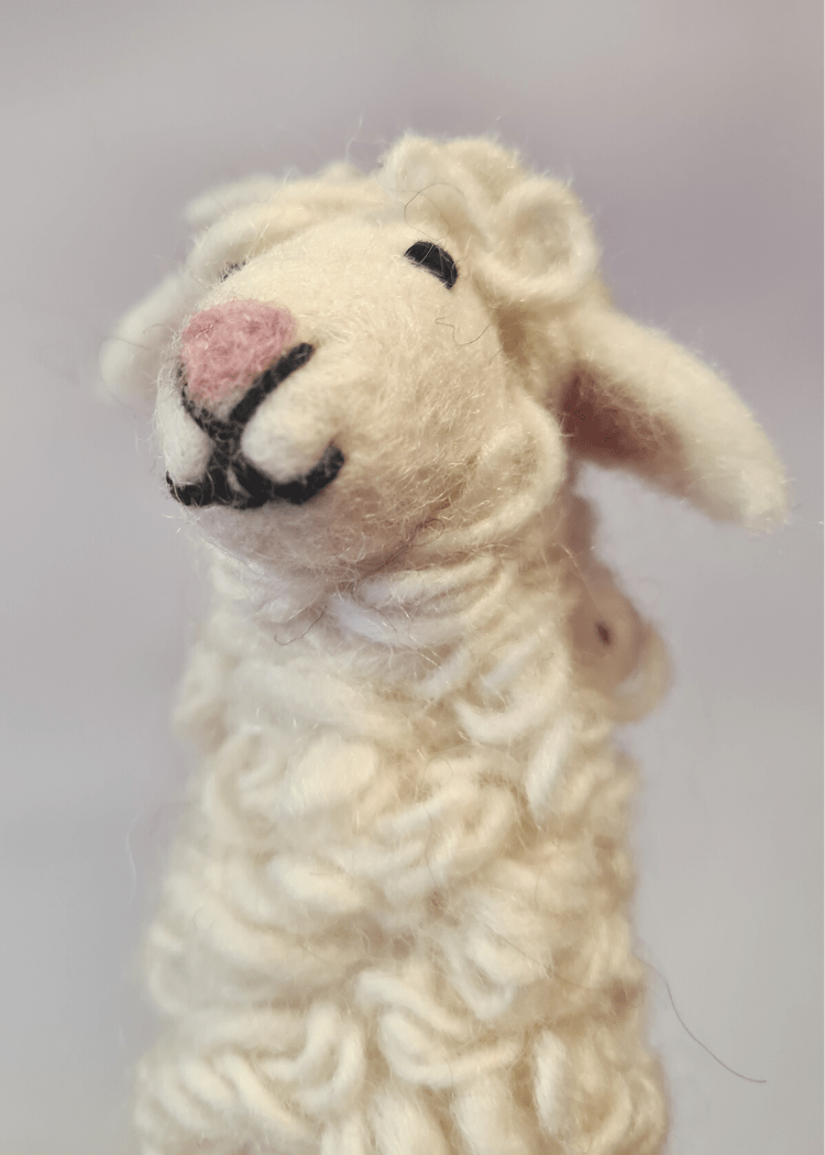 close up of white felt sheep finger puppet with pink nose and black thread smile and eyes