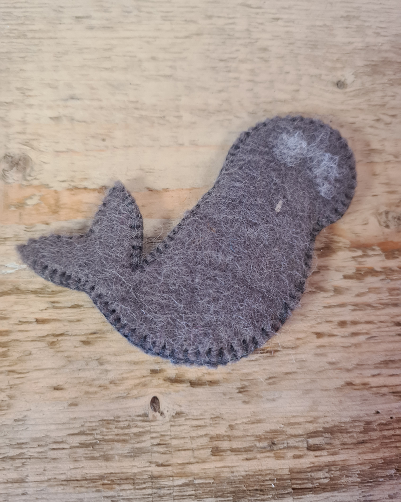 the back of a dark grey felt seal finger puppet with a sewn on smiley face on a wooden surface