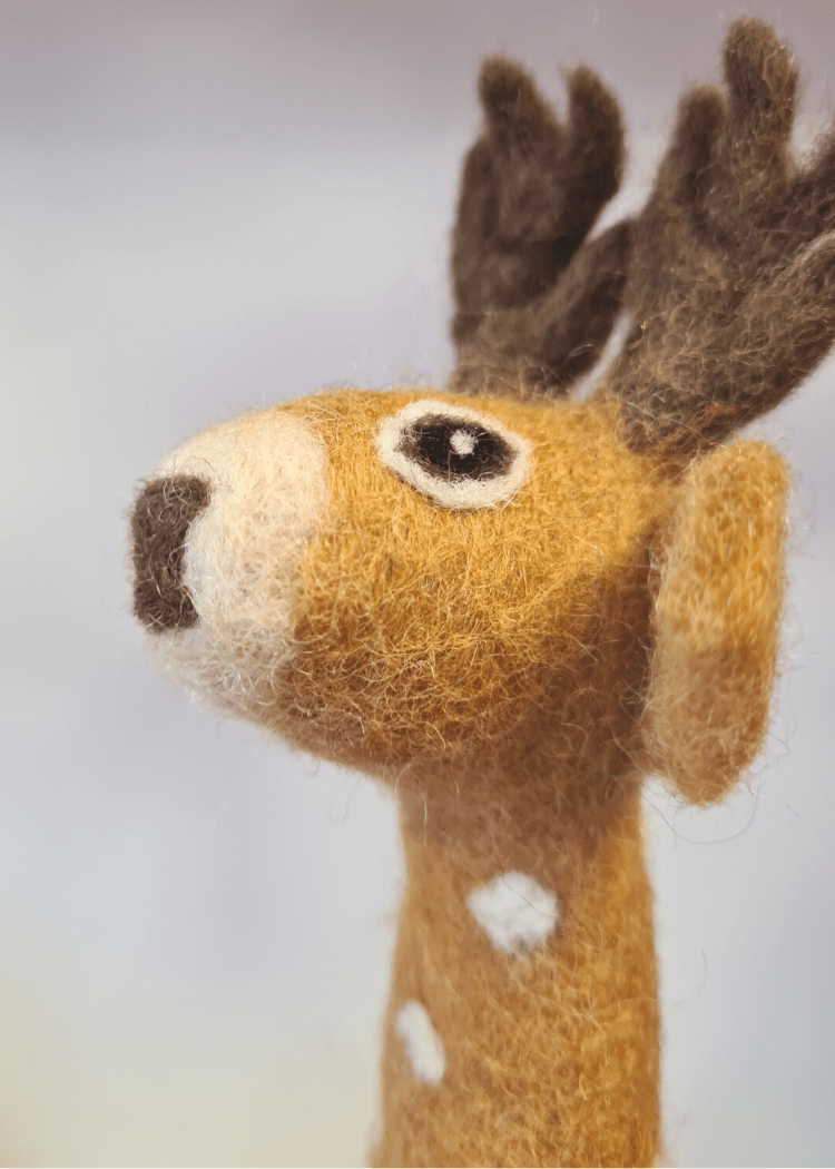 close up of a tan brown felt finger puppet with white spots and dark brown antlers and nose