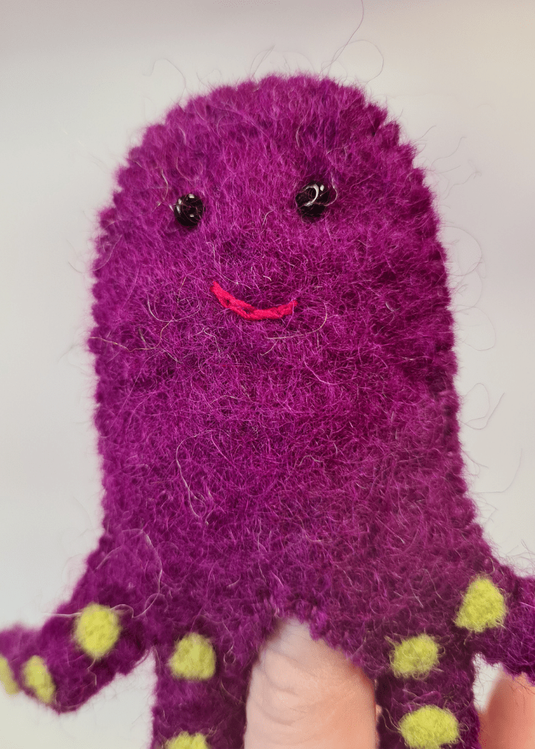 close up of purple felt octopus finger puppet with yellow spots and smiley face with beads on someones finger