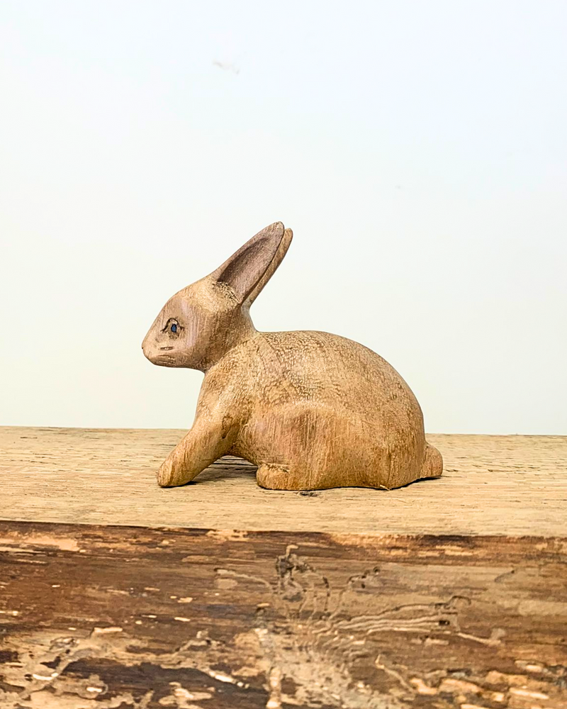 side view of carved wooden rabbit ornament sat on a wooden surface