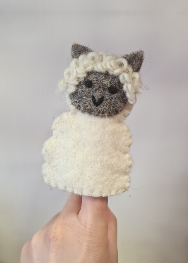 felt white sheep finger puppet with cute grey face sat on someones finger