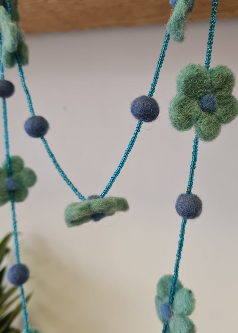 Blue pom pom flower necklace with beads hanging with close up of flower