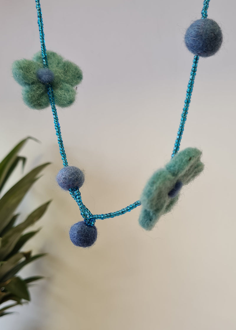 Blue pom pom flower necklace with beads hanging with close up of clasp