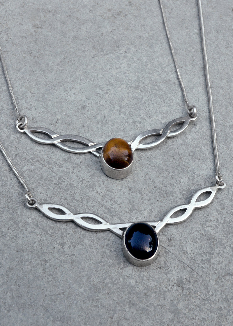 two silver celtic twist necklaces resting on a grey surface - one with a tigers eye stone and the other black onyx