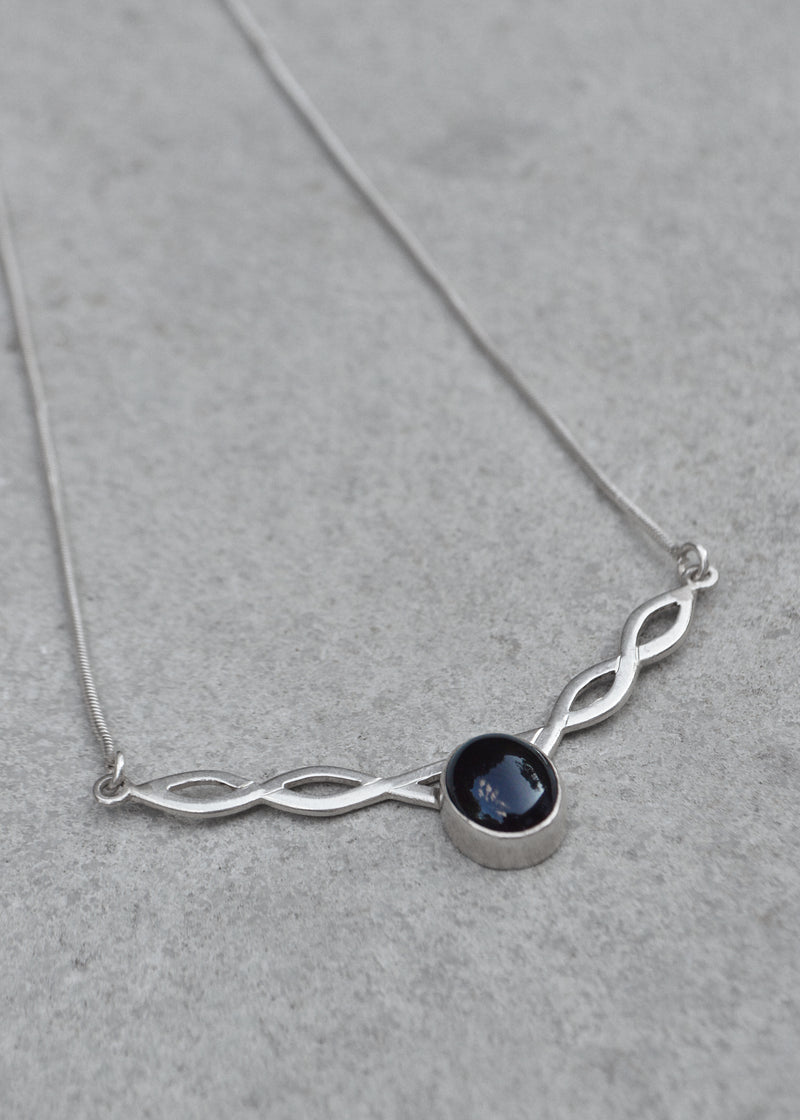 silver celtic twist necklace with black onyx stone resting on a grey surface