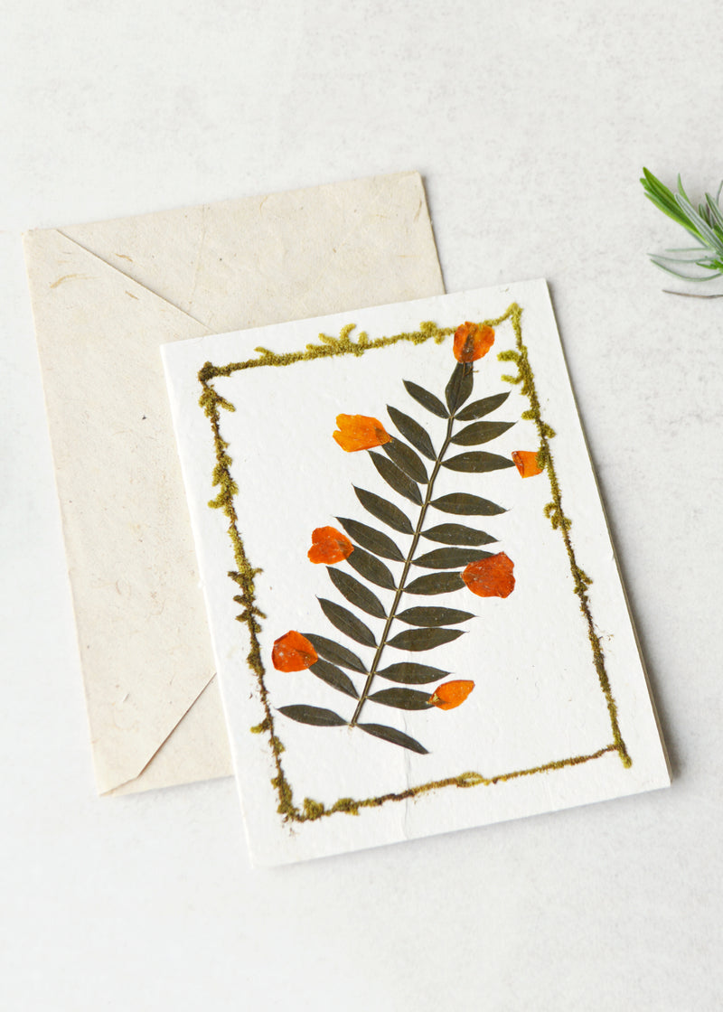 lokta paper greetings card with a dried flower on the front laid next to an envelope