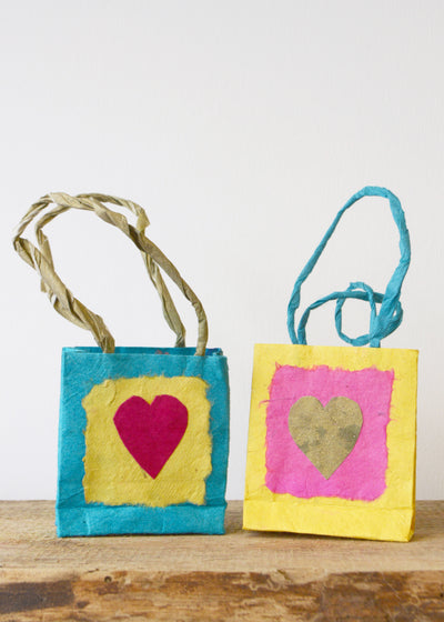 two small different coloured lokta paper gift bags with love hearts on sat on a wooden surface