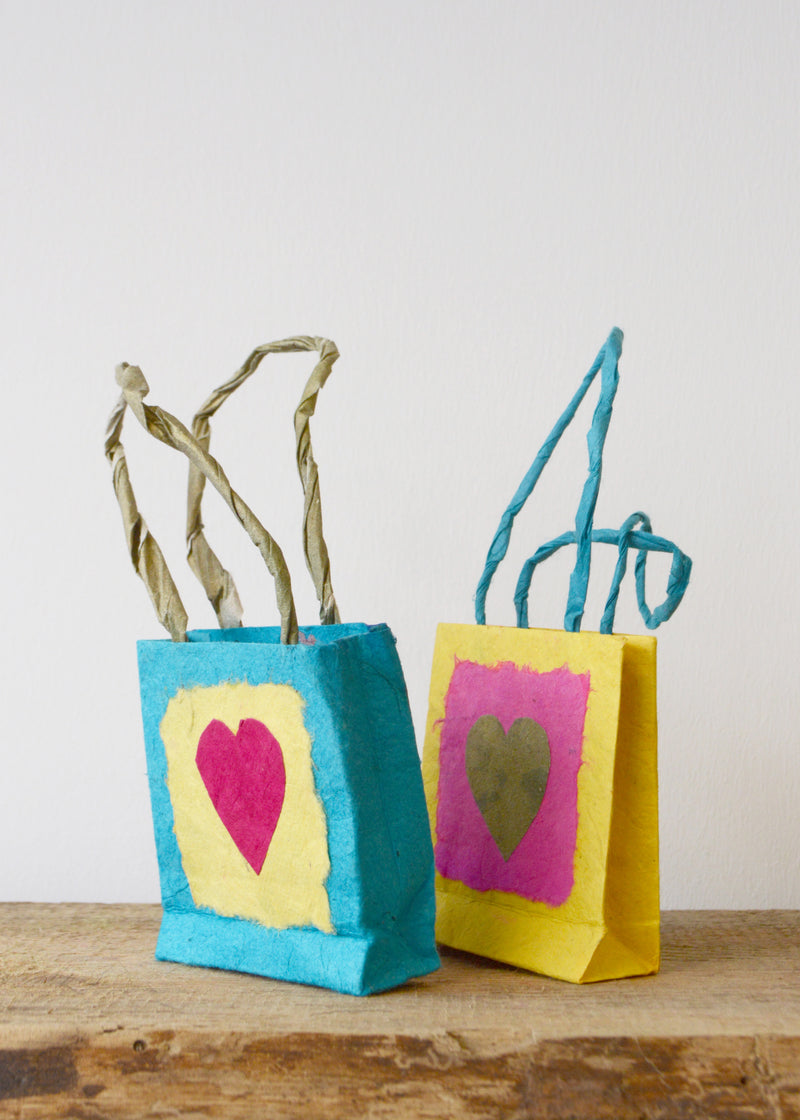 side view of two small different coloured lokta paper gift bags with love hearts on sat on a wooden surface