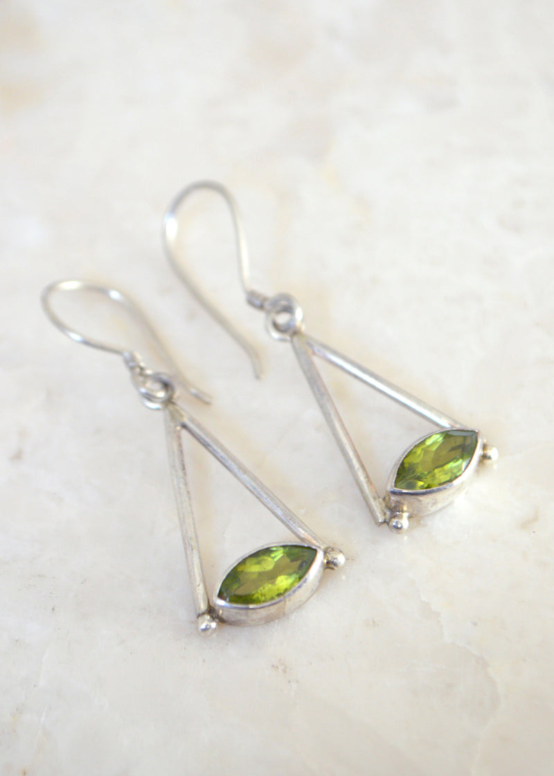 Silver marquise peridot earrings laid on a white marble surface