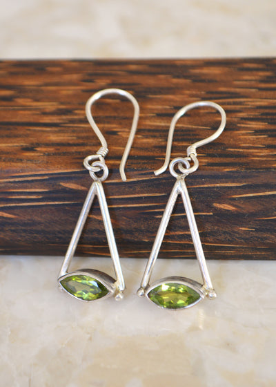Silver marquise peridot earrings resting on a wooden block on a white marble surface
