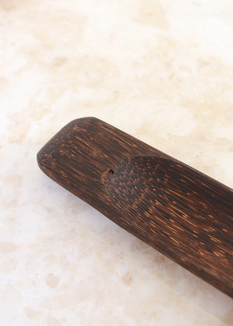 close up of a coconut palm wood incense holder laid on a marble surface