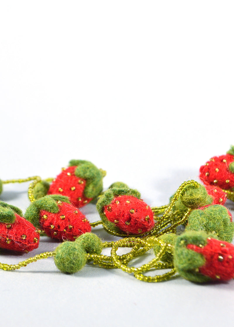 close up of strawberries, beads and pompoms from a red and green felt strawberry necklace with beads and pompoms bunched together in a pile