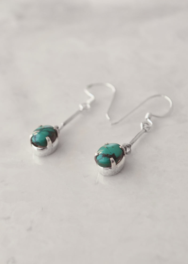 side view of Silver Turquoise Pole Earrings laying on a white marble surface