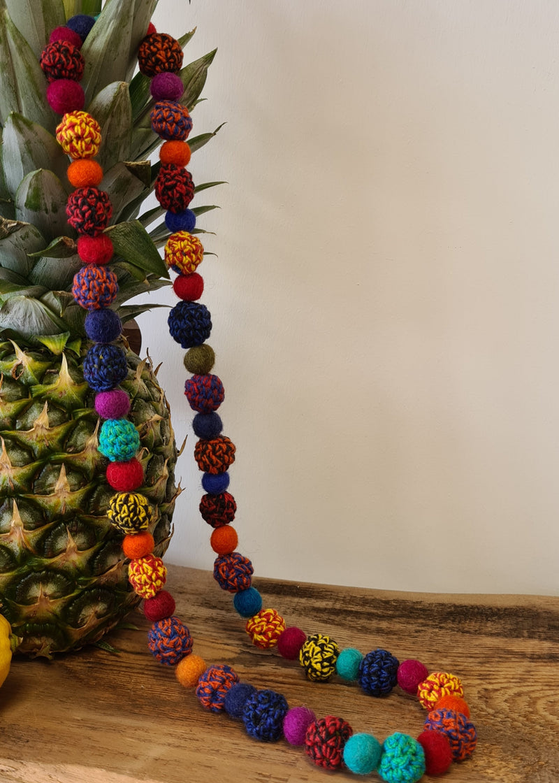 Large Felt Multi Colour Pom Pom Necklace draped over a pineapple