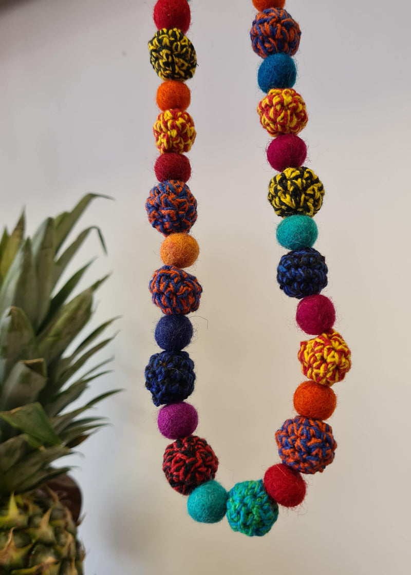 Large Felt Multi Colour Pom Pom Necklace hanging next to pineapple
