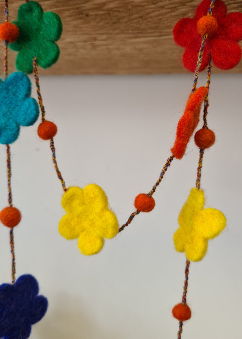 multi-colour felt pom pom flower necklace hanging from a block of wood