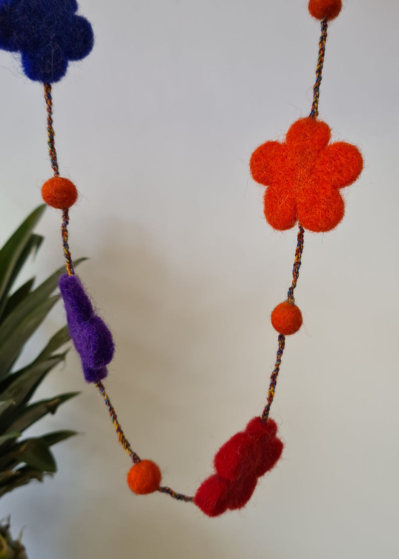 multi-colour felt pom pom flower necklace hanging next to a pineapple