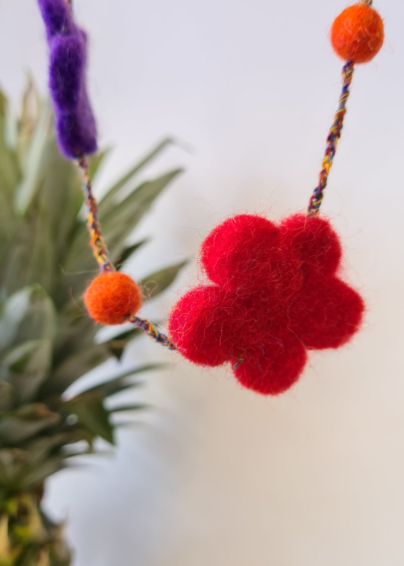 close up of red flower on a hanging multi-colour felt pom pom flower necklace