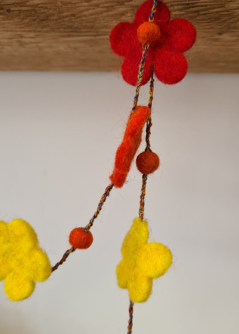 close up of flowers and pom poms on a multi-colour felt pom pom flower necklace hanging from a block of wood