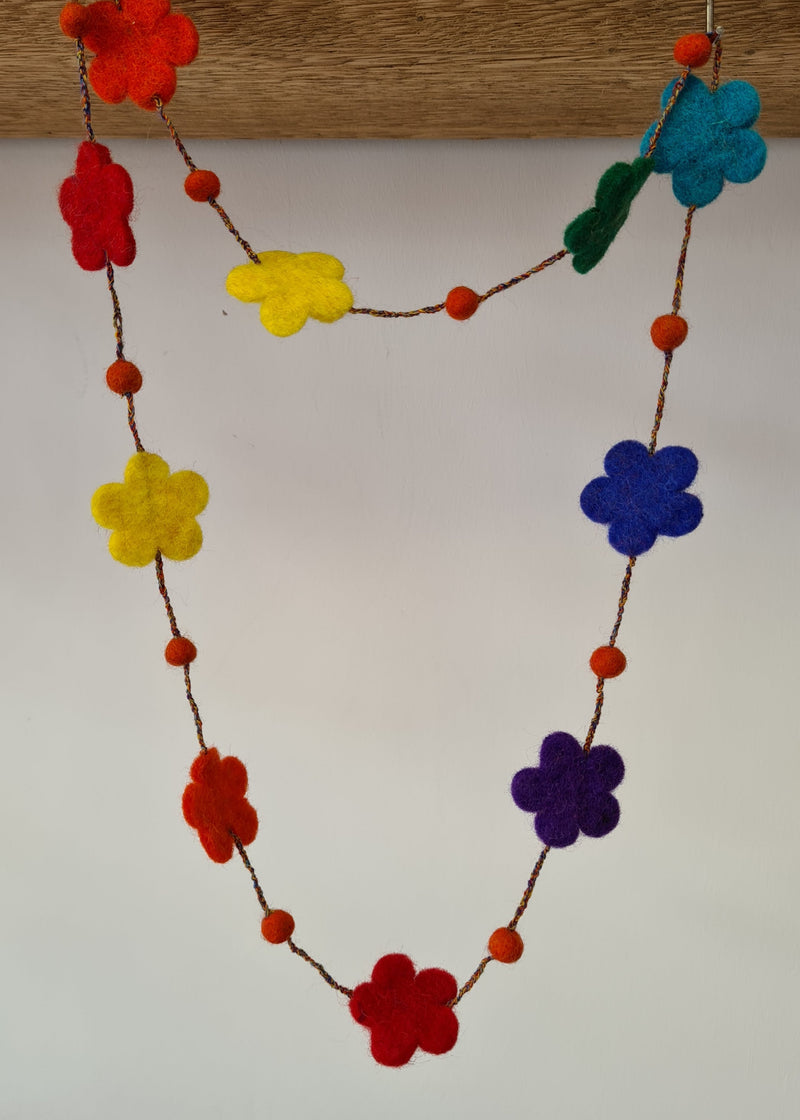 multi-colour felt pom pom flower necklace hanging from a block of wood