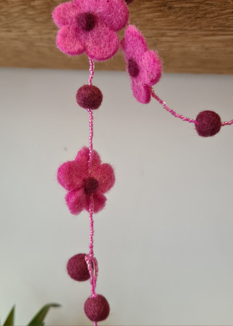 close up of Pink pom pom flower necklace with beads hanging from a block of wood