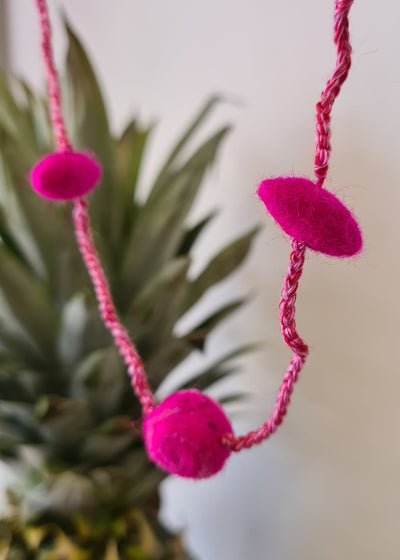 close up of Pink Pom Pom Felt Necklace with blurred pineapple in the background