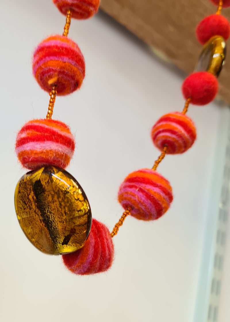 Red Felt Pom Pom Necklace with swirl detail hanging and close up of brown murano style glass pendant