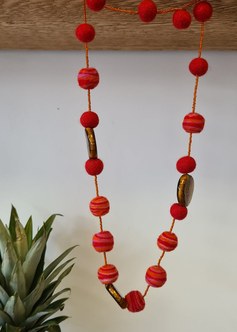 Red Felt Pom Pom Necklace with swirl detail  and brown murano style glass pendants hanging next to pineapple