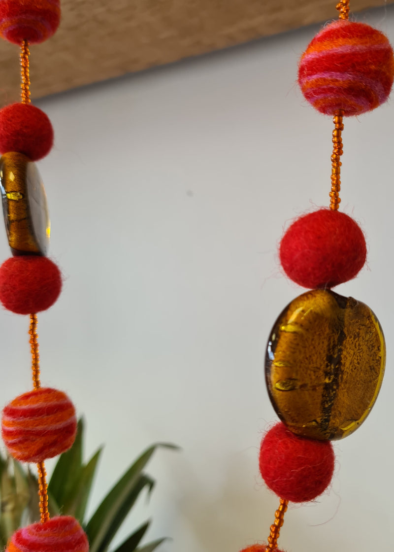 Red Felt Pom Pom Necklace with swirl detail hanging next to pineapple and close up of brown murano style glass pendant