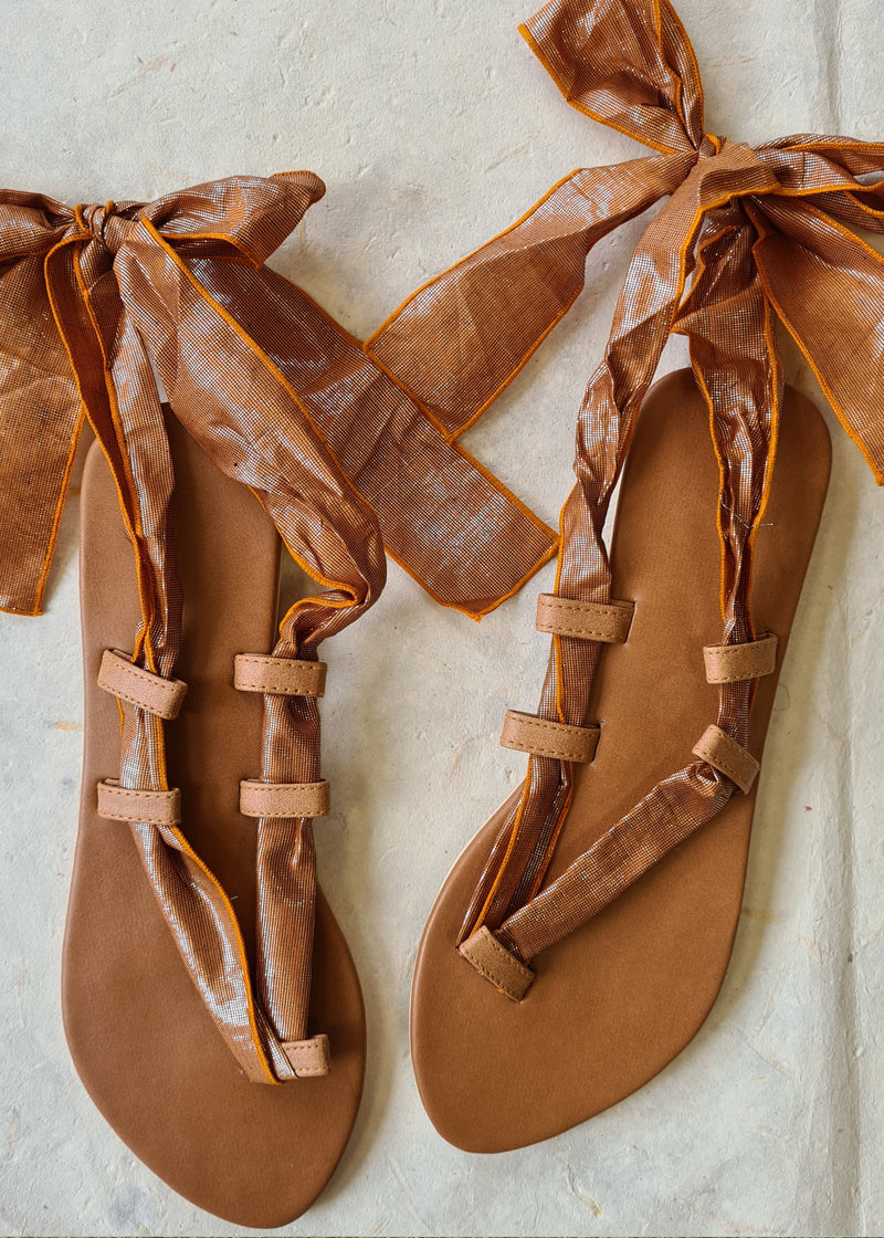 pair of brown metallic lace up sandals tied in a bow at the back
