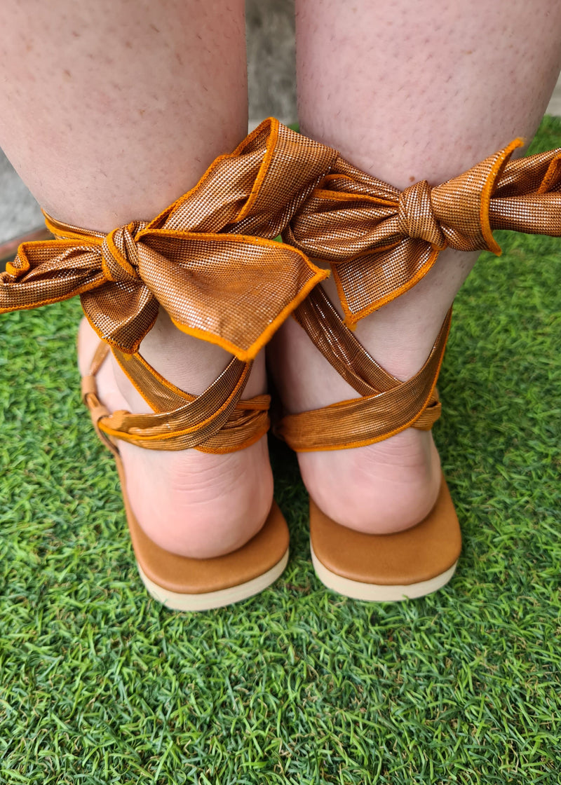woman wearing pair of brown metallic lace up sandals tied up in gladiator style with a close up of the bow at the back