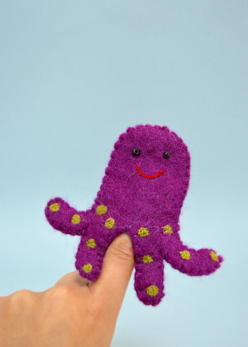 purple felt octopus finger puppet with yellow spots and smiley face with beads on someones finger with blue background