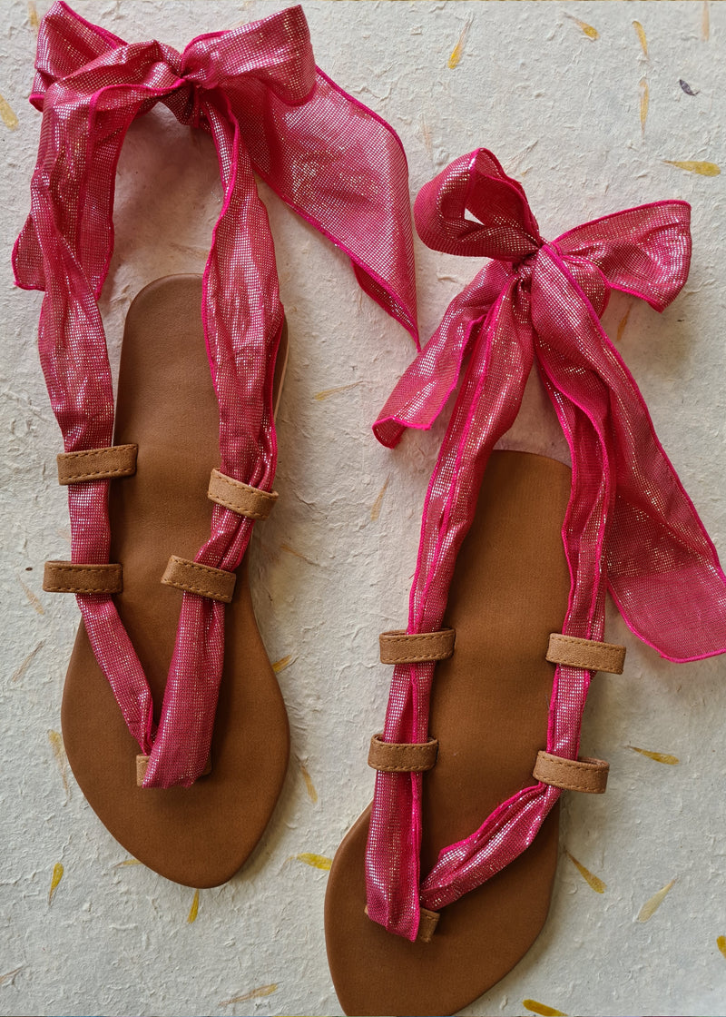 pair of pink metallic lace up sandals tied in a bow at the back