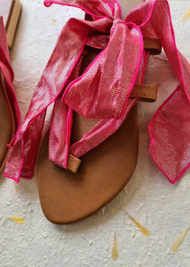 close up of pink metallic strap on lace up sandals tied in a bow
