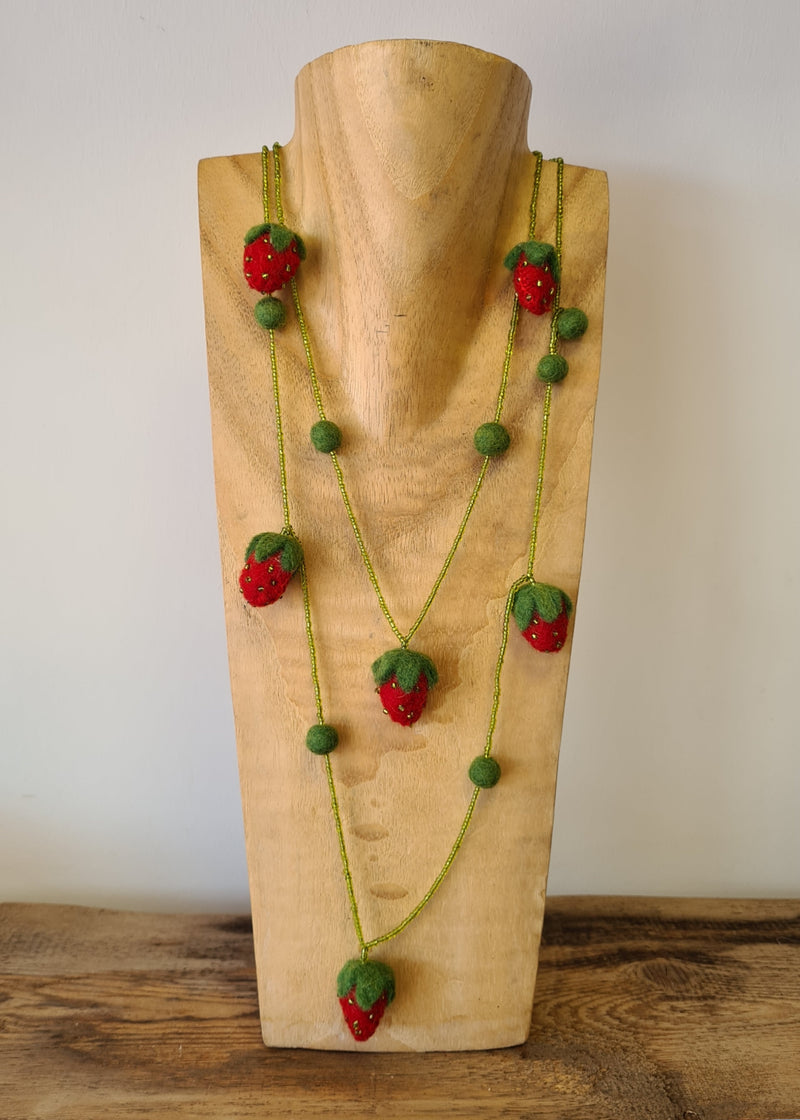 red and green felt strawberry necklace with beads and pompoms hanging on a wooden mannequin 
